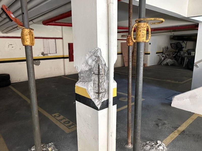 Nicho aberto em pilar de garagem com a armadura exposta, cercado por escoramento metálico