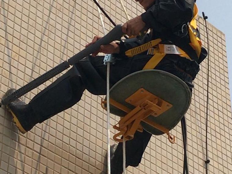 Técnico da HG Engenharia inspecionando fachada por cadeira suspensa, com capacete e cinto de segurança