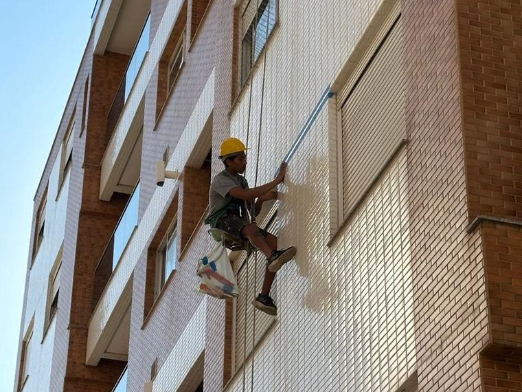 Profissional em cadeira suspensa vistoriando fachada de pastilha de um edifício