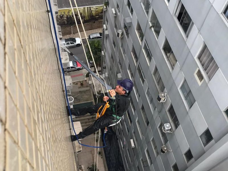 Profissional em acesso por corda fazendo hidrolavagem da fachada de um edifício em Florianópolis - SC